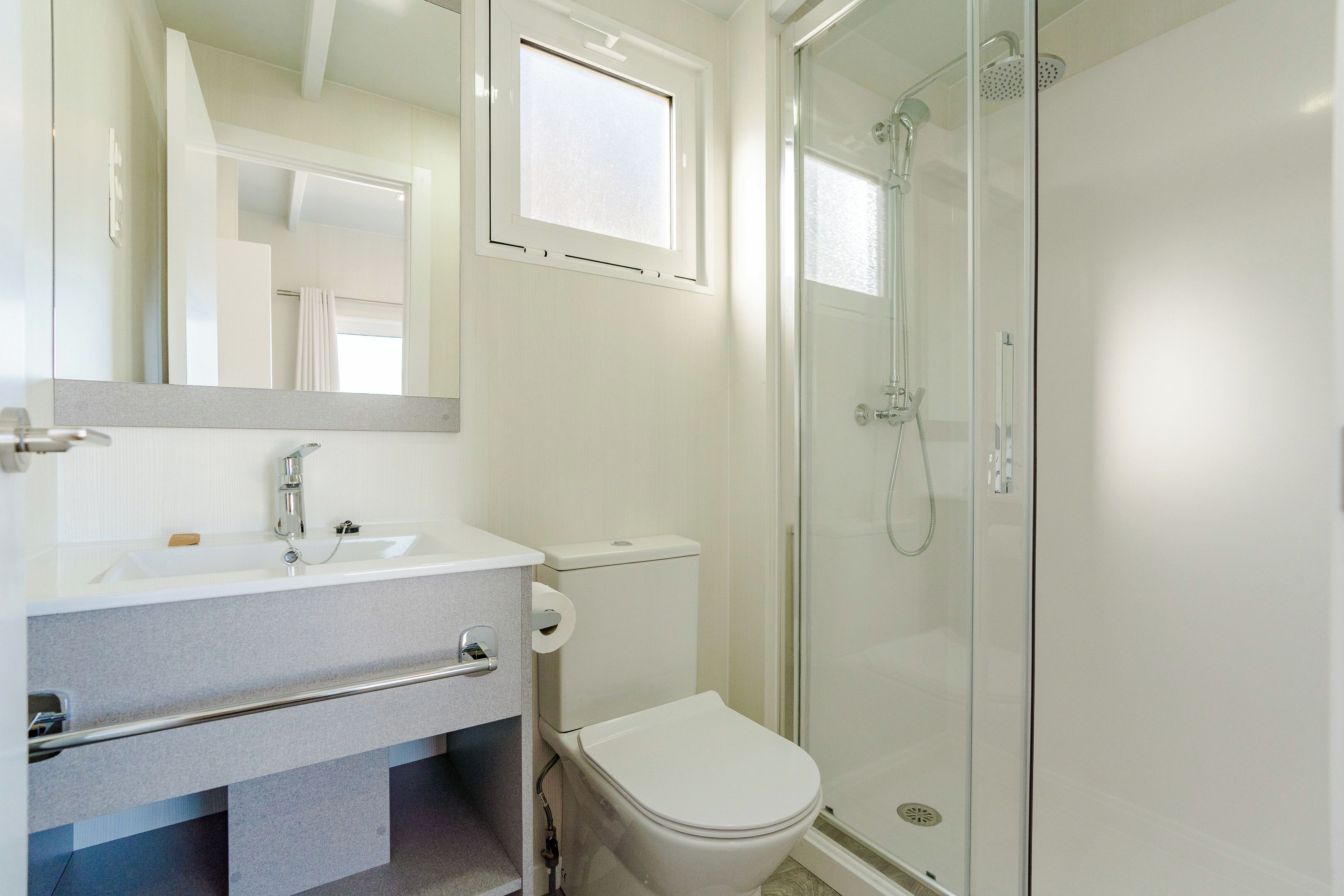 Une salle de bain moderne avec une douche à parois de verre, des toilettes blanches et un meuble-lavabo avec un miroir.