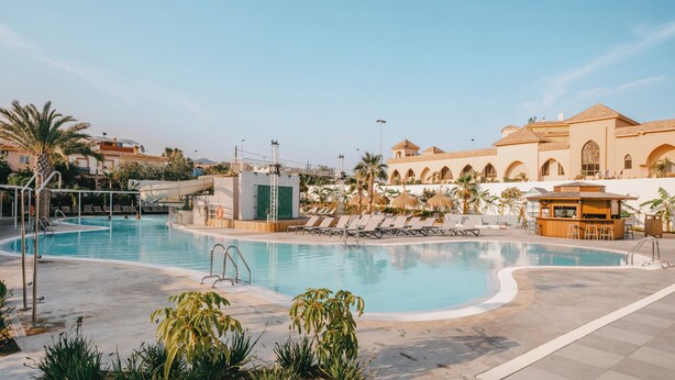 Zona de piscina con sillas de descanso, puesto de socorrista y zona de bar.
