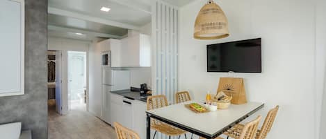 Una cocina moderna con armarios blancos, una mesa de comedor con sillas de mimbre y un televisor montado en la pared.