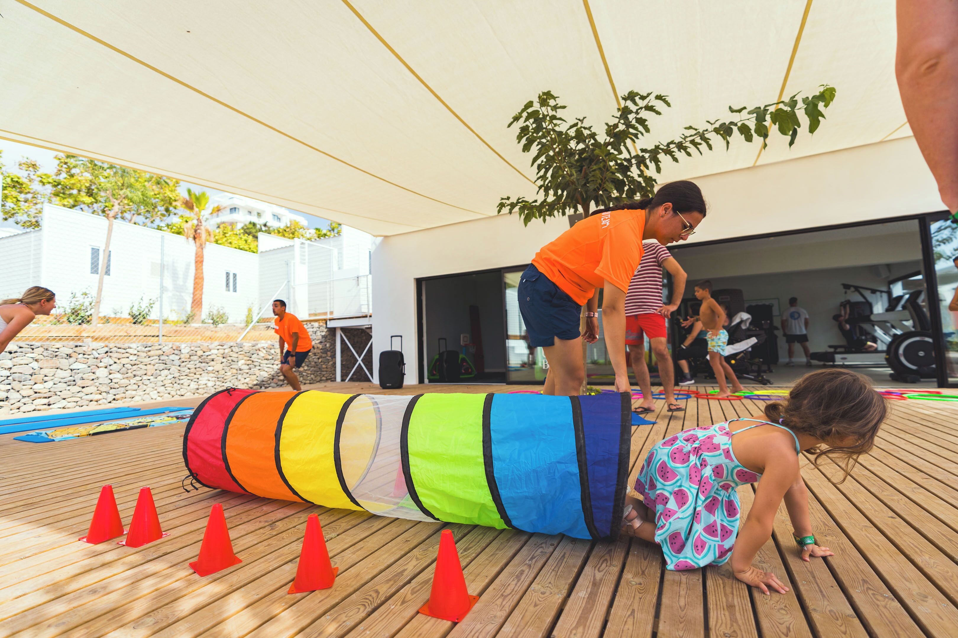 An outdoor wooden deck with a colorful obstacle course, including a large tube and red cones.