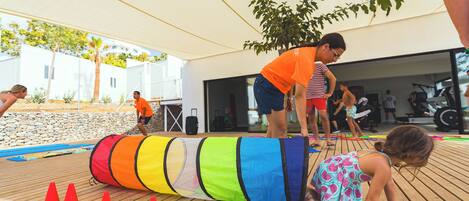 An outdoor wooden deck with a colorful obstacle course, including a large tube and red cones.