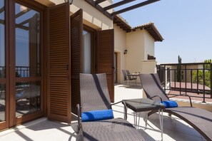 A balcony with two lounge chairs and a table, a sliding glass door, and a view of the building's exterior. - 2 Bedroom Apartment - AB11TH (Kouklia)