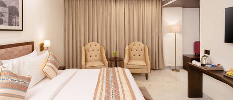 A hotel room with a large bed, two armchairs, a small table, a desk, and a television.