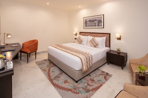 Habitación de hotel con cama, escritorio, silla, mesita de noche y una pequeña mesa con una planta.
