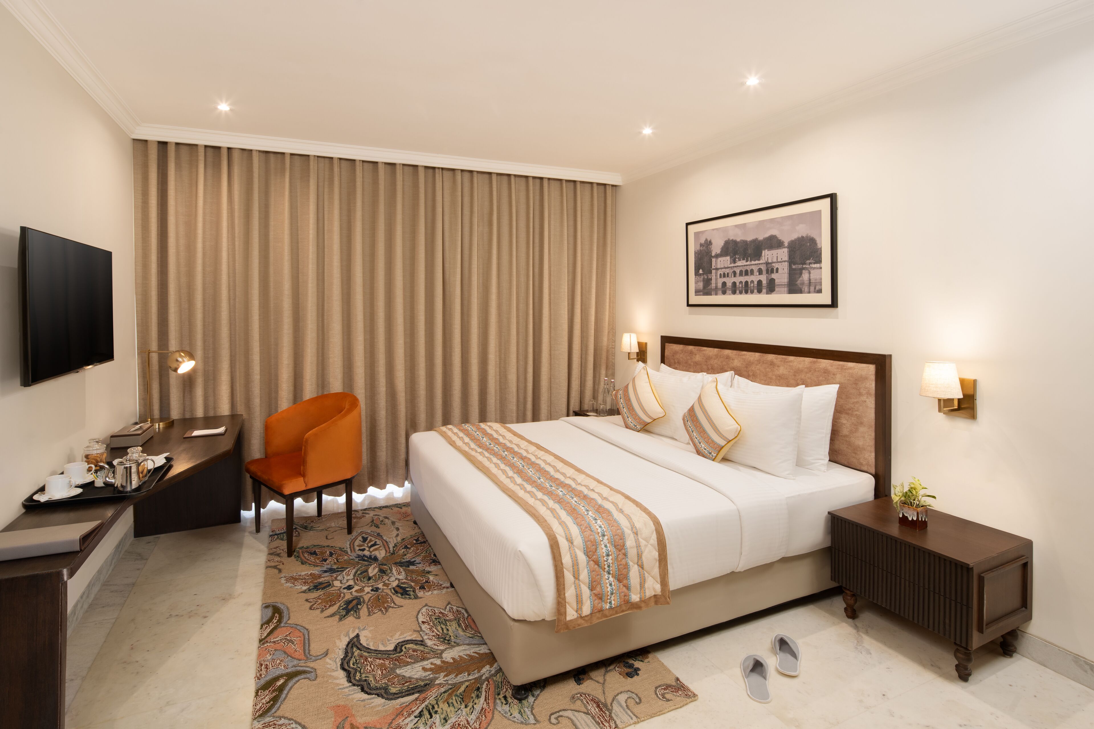Habitación de hotel con una cama grande, un escritorio, una silla, un televisor y un cuadro en la pared.