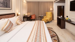 Une chambre d’hôtel avec un grand lit, un bureau, une chaise, un canapé, une télévision et une armoire.