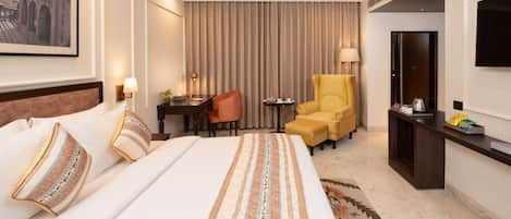 Habitación de hotel con una cama grande, un escritorio, una silla, un sofá, un televisor y un armario.