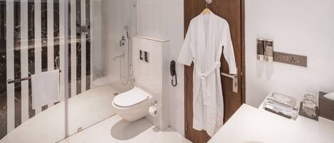 Un baño moderno con cabina de ducha de vidrio, un inodoro, una puerta de madera y una bata blanca colgada en la puerta.