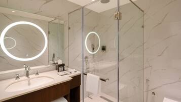 A modern bathroom with two sinks, a large mirror with a circular light, and a glass-enclosed shower area.