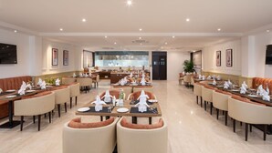 Un vaste espace de restauration dans l’hôtel, avec de nombreuses tables et chaises, un bar central et des œuvres d’art encadrées qui ornent les murs.