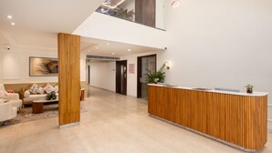 Un espace d’accueil moderne, avec un comptoir de réception en bois, un coin salon comprenant un canapé et des fauteuils, et une grande œuvre d’art encadrée accrochée au mur.