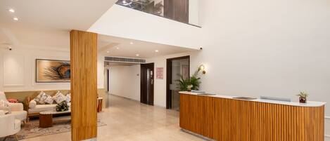 A modern reception area with a wooden reception desk, a seating area with a sofa and chairs, and a large framed artwork on the wall.