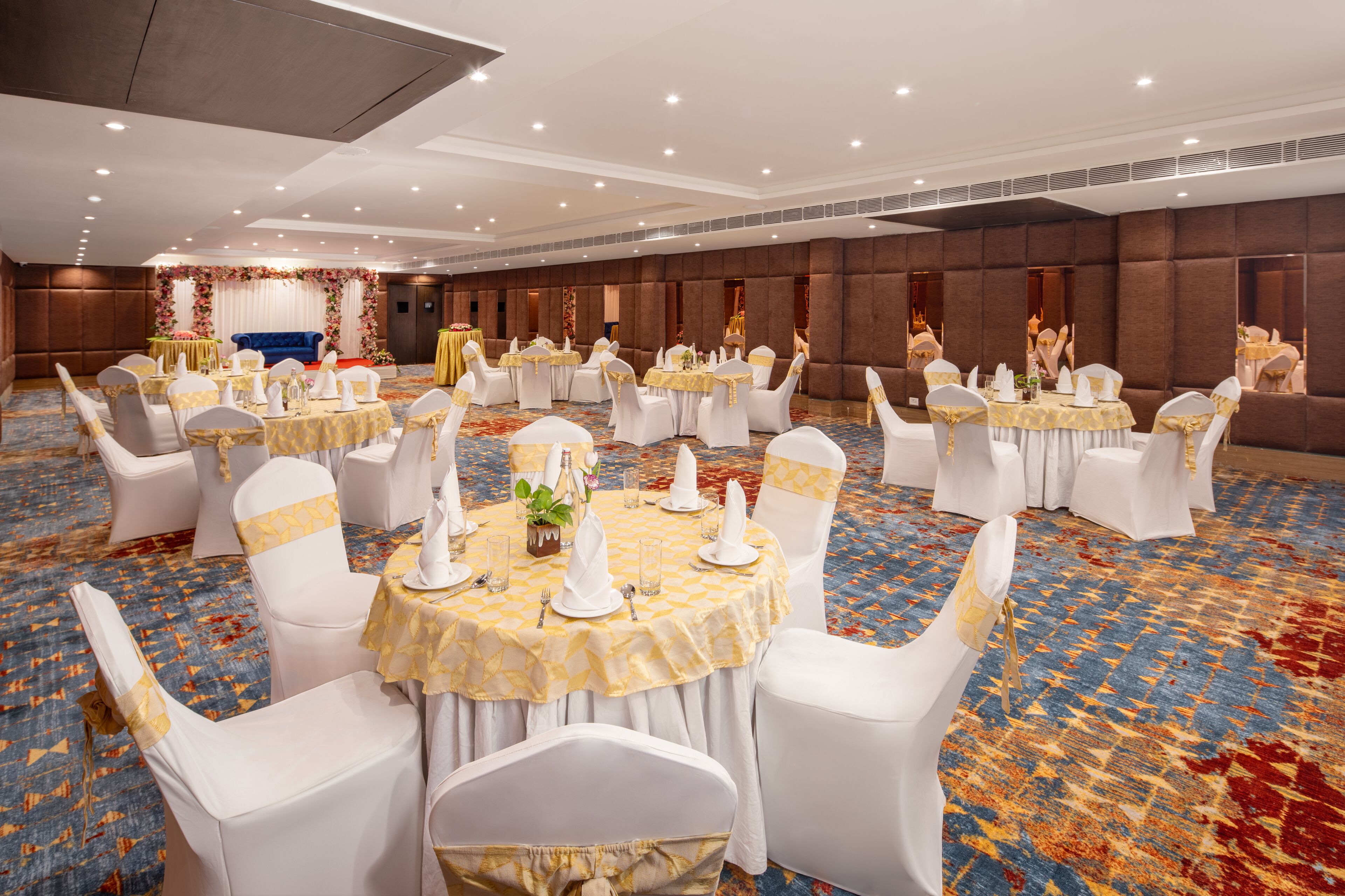 A banquet hall with round tables, white chairs, and a stage with floral decorations.