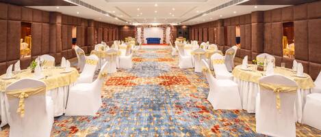 A banquet hall with rows of tables, white chairs, and a central stage.