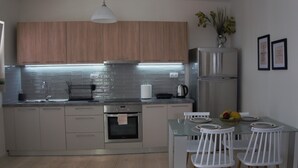 A modern kitchen with wooden cabinets, a stainless steel refrigerator, and a glass dining table with white chairs.