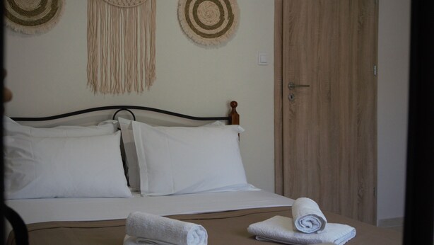 A neatly made bed with white linens, two decorative wall hangings, and a wooden door in the background.
