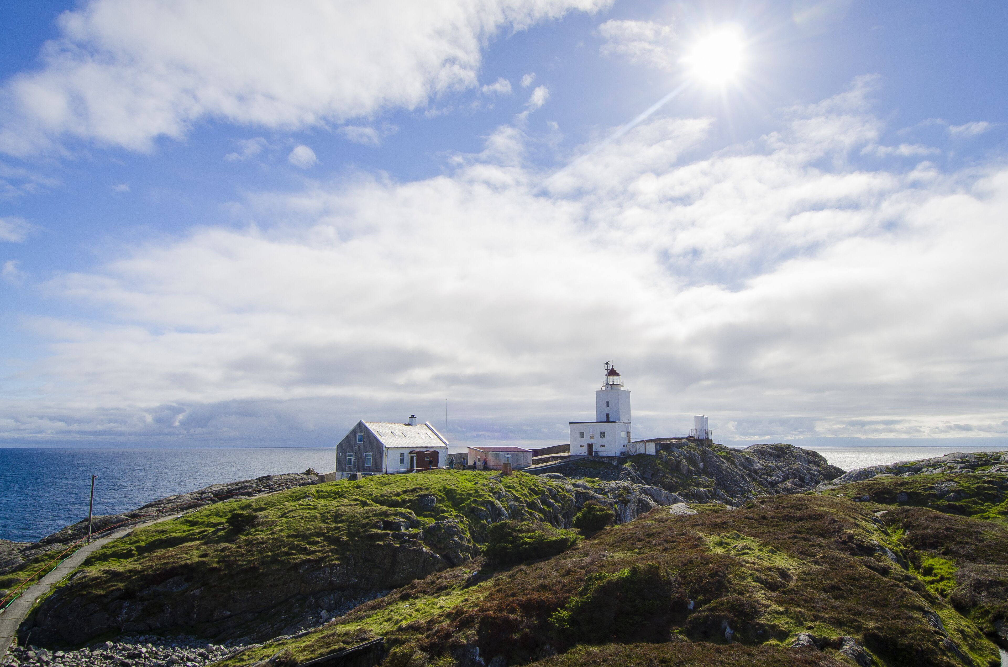 Un paysage côtier avec un phare, un petit bâtiment blanc et un terrain rocheux.