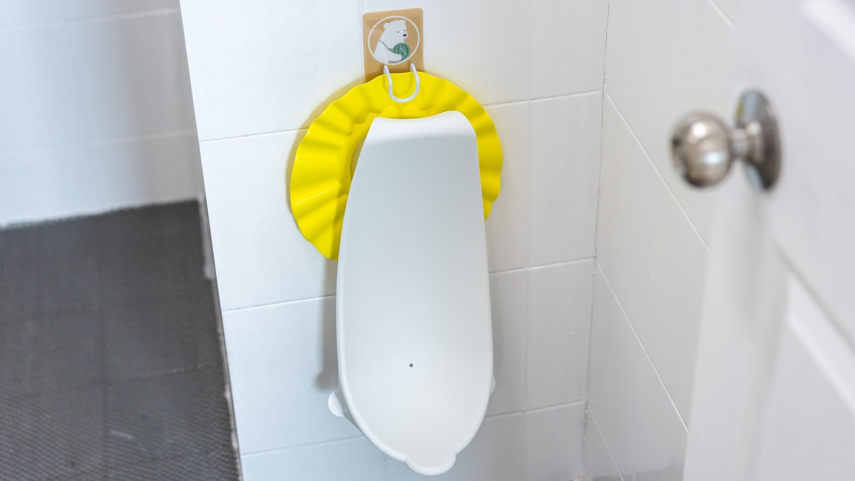 A urinal with a yellow privacy cover and a soap dispenser on the wall.