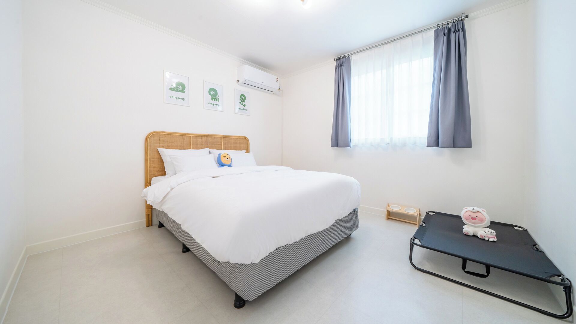 A bedroom with a bed, a small bedside table, a window with curtains, and wall-mounted air conditioning.