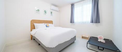 A bedroom with a bed, a small bedside table, a window with curtains, and wall-mounted air conditioning.