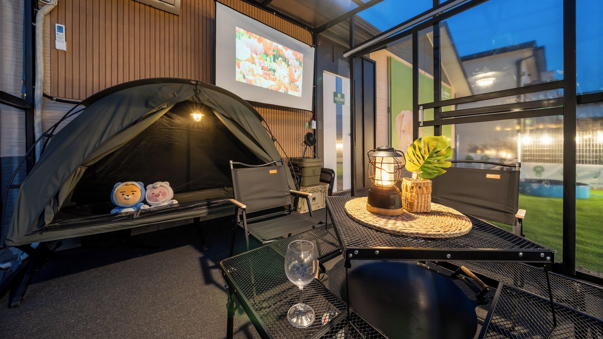 Un espacio al aire libre con carpas, una mesa, sillas, un farol y una copa de vino.