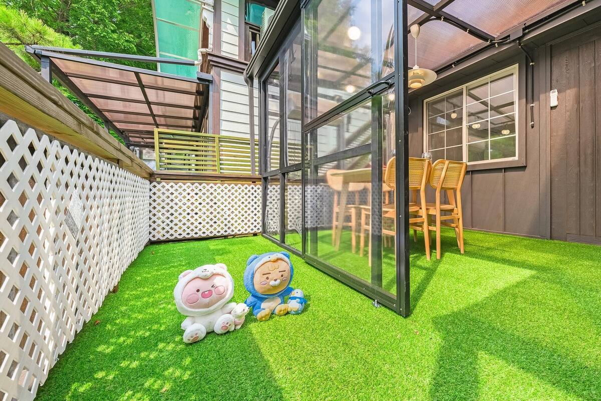 Ein Garten mit Kunstrasen, einem weißen Spalierzaun und einer Glastür, die auf eine Holzterrasse führt.