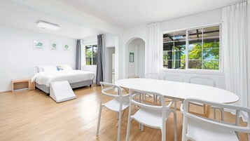 Habitación de hotel con cama, una mesa y sillas, una ventana con cortinas y vistas a zonas verdes.