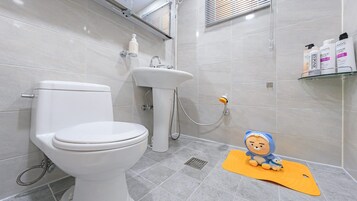 Un baño con inodoro, lavamanos y ducha. Hay artículos de aseo en una repisa.