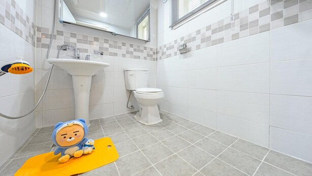 Ein Badezimmer mit Waschbecken, Toilette und Dusche. Auf dem Boden liegt eine gelbe Matte und ein Plüschtier.