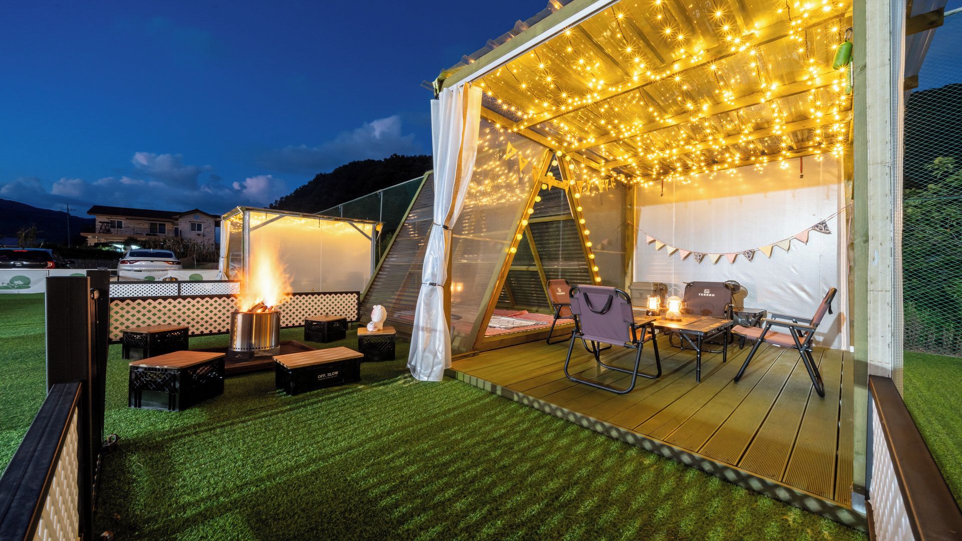 A tented outdoor area with a fire pit, seating, and string lights.