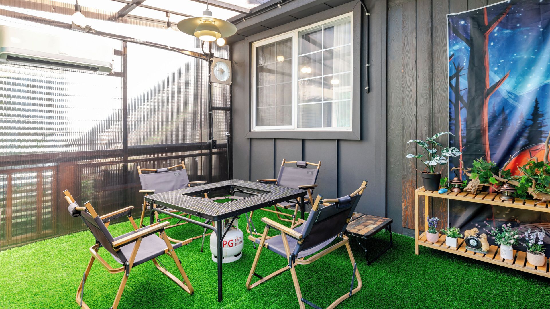 Un patio con una mesa, sillas, una estantería con plantas en macetas y un ventanal grande.