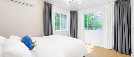 Ein modernes Hotelzimmer mit einem großen Bett, zwei Fenstern mit Vorhängen, einer Deckenleuchte und einer Klimaanlage.