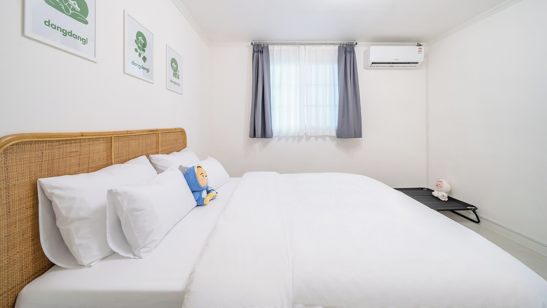A hotel room with a bed, a window with curtains, an air conditioning unit, and wall-mounted artwork.