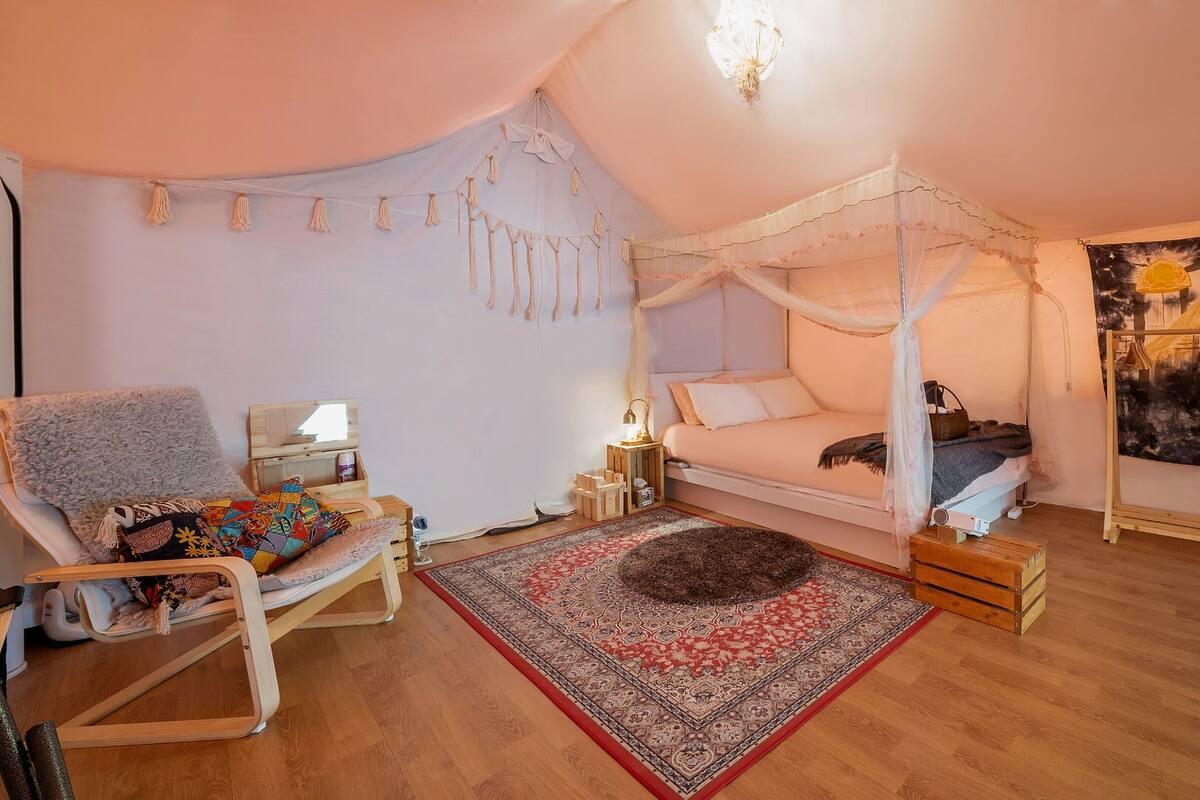 Un dormitorio acogedor con una cama con dosel, una silla de madera, una mesita de noche pequeña y un tapiz grande en la pared.