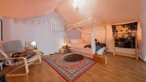 Une chambre confortable avec un lit à baldaquin, une chaise en bois, une petite table de chevet et une grande tapisserie au mur.