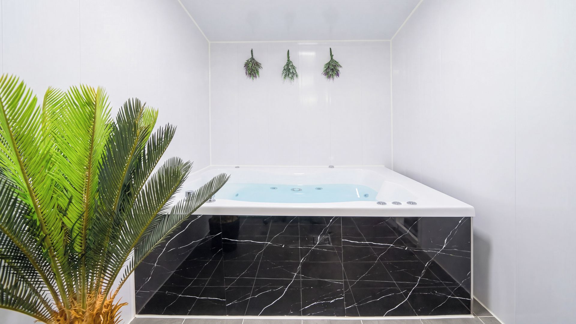 Un baño moderno con una bañera de mármol negro, pared con azulejos blancos y una planta de palma en maceta.