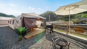 Ein zeltschattiges Außenbereich mit Grill, Sitzgelegenheiten und Blick auf die umliegende Landschaft.