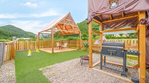 Une terrasse en bois avec un barbecue, un espace salon abrité et un petit terrain de football.