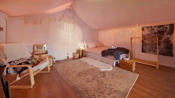 Un dormitorio acogedor con una cama, una silla, una mesita y un tapiz en la pared.