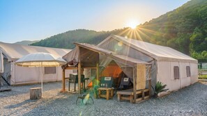 A series of tents with a covered seating area and tables, set on a gravel ground with a mountainous backdrop. - Gapyeong Iluglamping (Gapyeong)