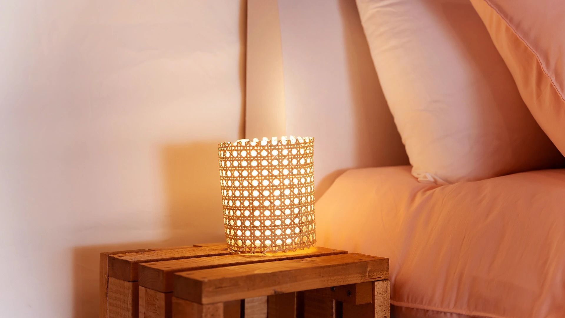 Une table de chevet en bois sur laquelle repose une lampe cylindrique perforée.