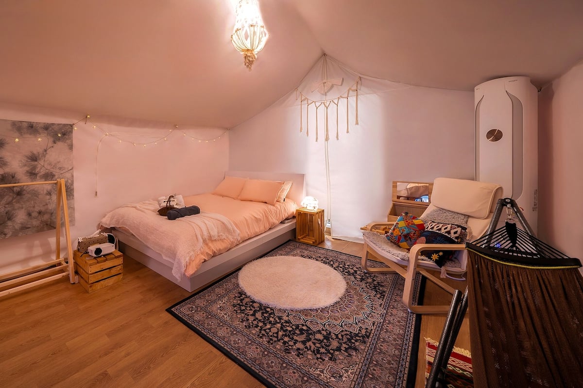 Un dormitorio acogedor con cama, mesitas de noche, una silla y un sillón colgante, adem ás de un ventanal grande.