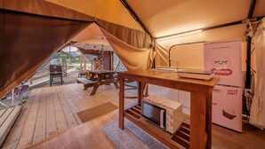 Een gezellige tent met een houten tafel en bank, een koelkast en uitzicht op de natuur.