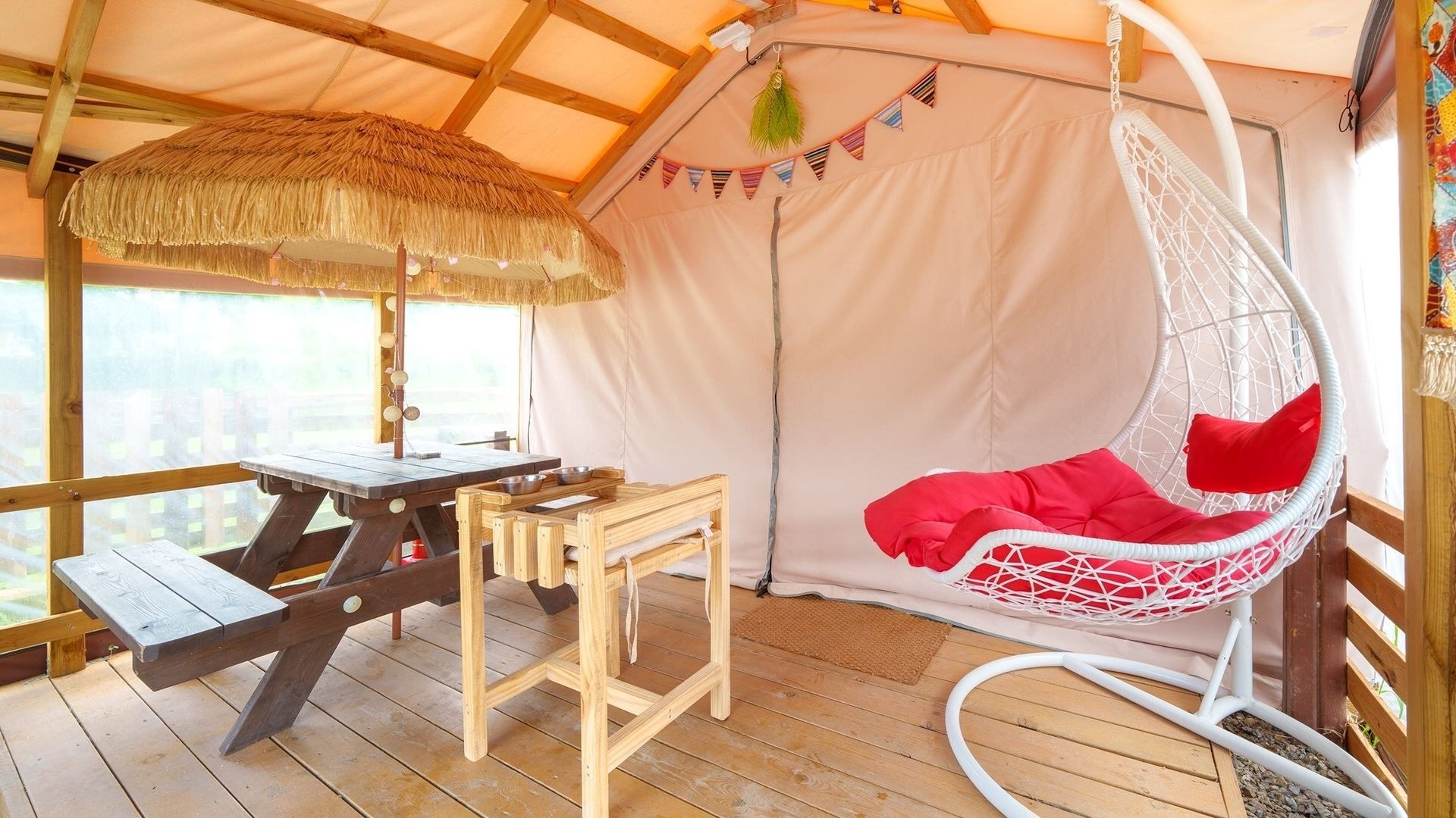 Una carpa con una mesa de madera y un sillón colgante.