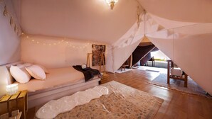 Een knus slaapkamer met een bed, een hanglamp, een schilderij en een tentachtige constructie.