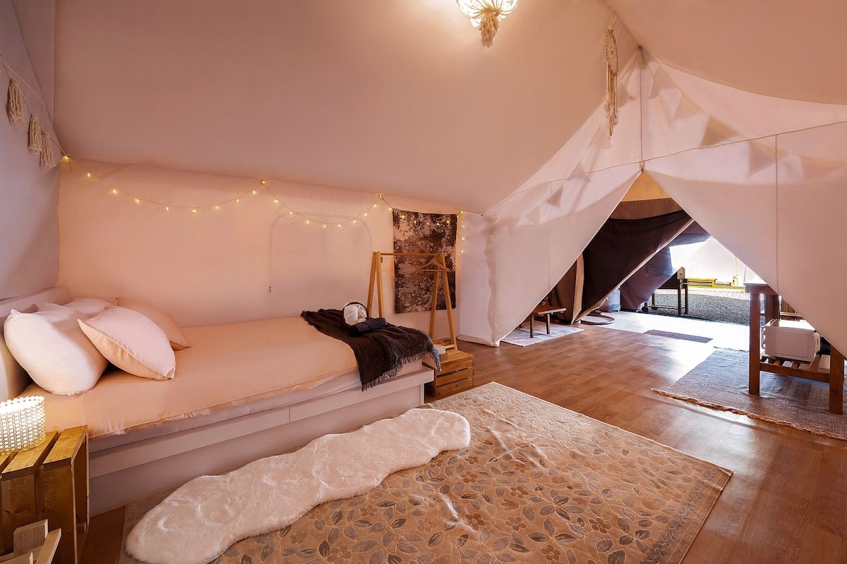 Un dormitorio acogedor con cama, una lámpara colgante, un cuadro y una estructura tipo tienda.