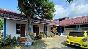 A two-story house with a tiled roof, potted plants, and a yellow car parked in the driveway. - Hotel O Lies Kostel Syariah (Kendal)