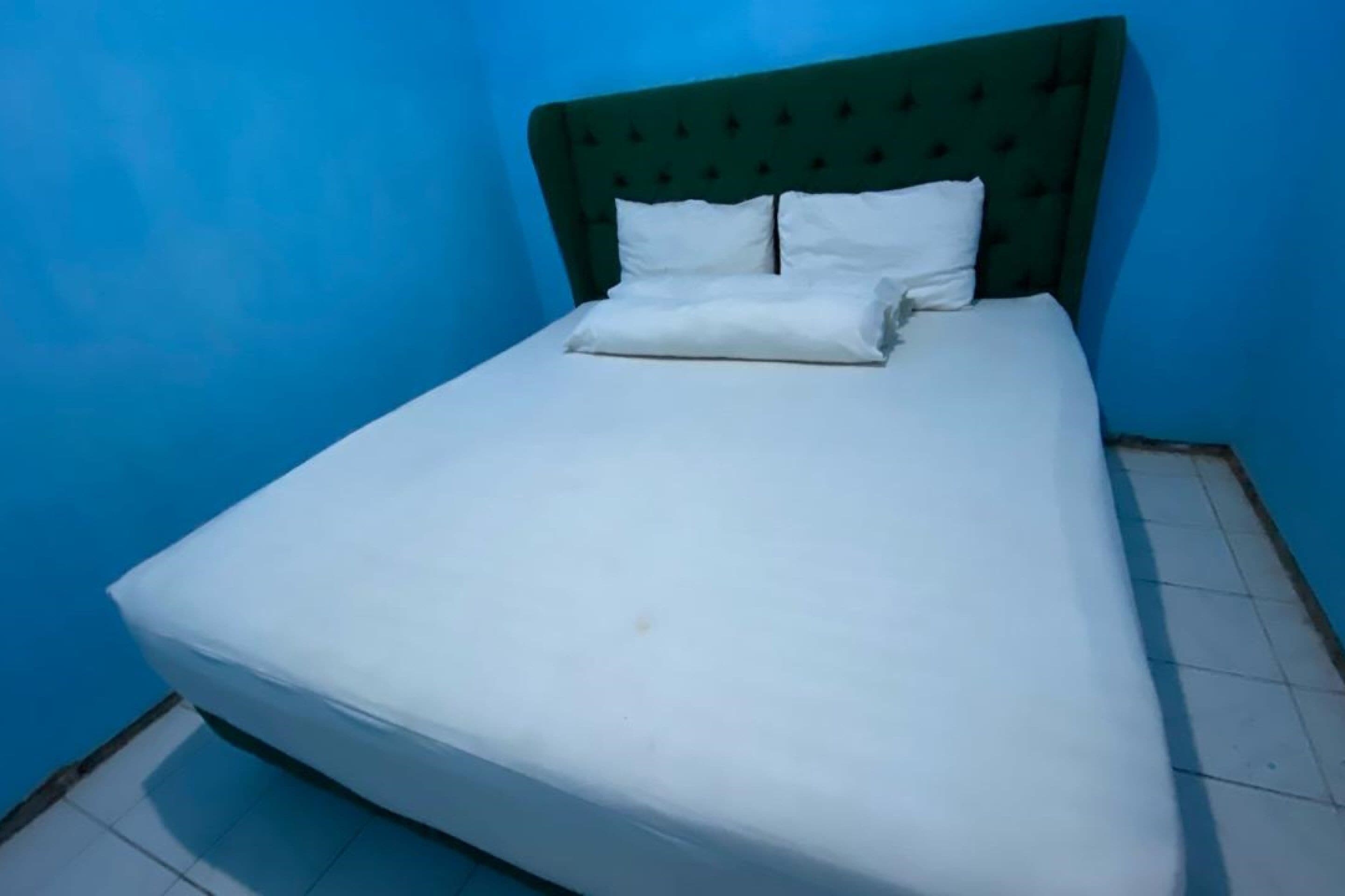 A single bed with a green upholstered headboard, white bedding, and a tiled floor.