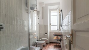 A narrow, modern bathroom with a bathtub, toilet, and sink.