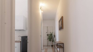 A hallway with patterned flooring, a door leading to a kitchen, and a small table with a plant.